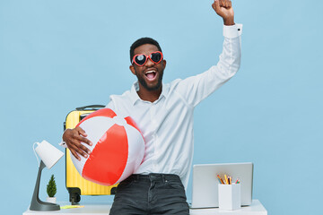 Cheerful young man with sunglasses holding beach ball in bright office setting, celebrating...