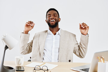 Smiling happy young African American man in beige blazer and white shirt enjoying success at work...