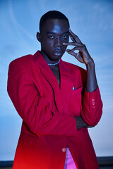 Elegant young man showcasing fashion in a striking red suit under a dynamic blue backdrop
