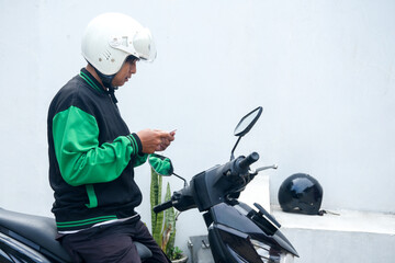 Male Delivery Driver Checking Smartphone For Order While Seated On Motorcycle