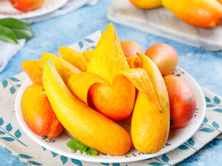 Fresh Tropical Mango Slices and Whole Fruits on Decorative Plate with Blue Kitchen Setting