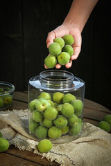 Fresh Green Yunnan Plums in Glass Jar for Wine Infusion and Preserving on Rustic Farm Kitchen Table