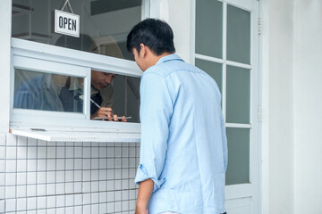 Rear View Of Young Man Using Digital Tablet To Place Order At Window