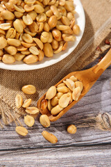 Roasted Salted Peanuts in Bowl and Wooden Spoon on Rustic Wood Background