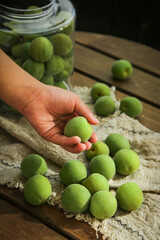 Fresh Green Plums on Rustic Wooden Table with Hand Holding Fruit