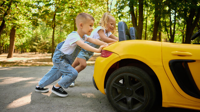 Children pushing toy yellow car together outdoors with joyful teamwork. Concept of collaboration, childhood play, outdoor activity, and teamwork learning with happiness.