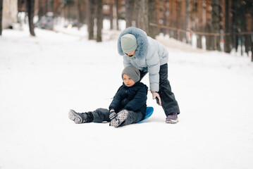 Sister helping brother sitting on sled in snowy park during winter day
