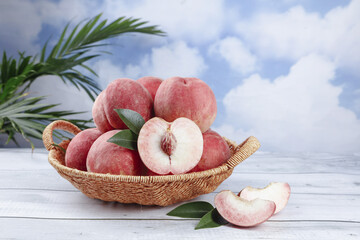 Fresh Peaches in Wicker Basket on White Wood Table with Palm Leaves and Blue Sky Background