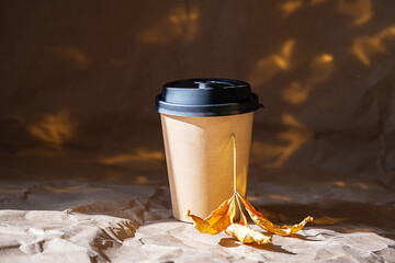 Kraft paper cup with black lid and yellow autumn leaf. Fall coffee drink concept