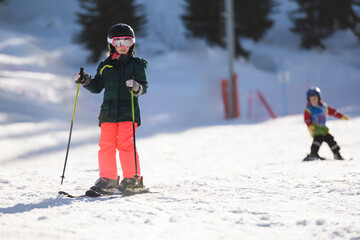 Young girl skiing on sunny snowy slope with another child skiing in background