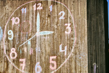 Horloge dessinée à la craie colorée sur une colonne de béton indiquant trois heures.