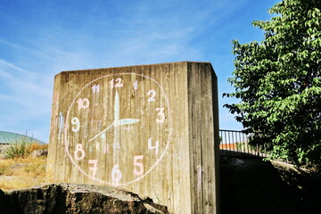 Horloge dessinée à la craie colorée sur une colonne de béton indiquant trois heures.