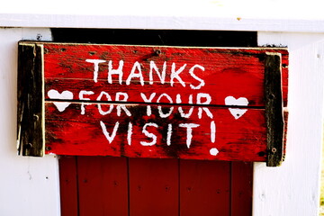 Thanks for your visit! (Merci de votre visite!). Inscription blanche en anglais sur fond rouge sur un panneau de bois.