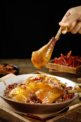 Hand Holding Glazed Chicken Drumstick Over Spicy Chongqing Chinese Dish with Sesame Seeds and Red...