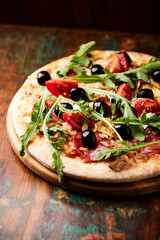  Pizza with salami, tomatoes and mozzarella cheese, black olives and arugula. Rustic wooden background. Soft focus. 