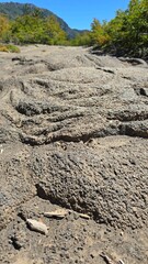 Close-up of textured volcanic trail with erosion marks in a forested mountain landscape under a bright blue sky. Ideal for geology, travel, hiking, terrain texture, and nature backgrounds.