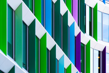 Colorful office building façade with angled window panels in green, purple, and blue geometric...