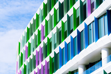 Colorful office building façade with angled window panels in green, purple, and blue geometric...
