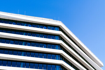 Contemporary office building with reflective blue windows, white façade, and minimal yellow...