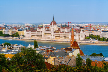 Obraz premium Budapest Parliament building on the Danube river with cityscape and historical architecture under clear sky.