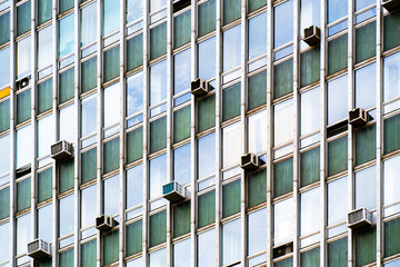 Old office building façade with repetitive window pattern, aged green panels, and visible air...