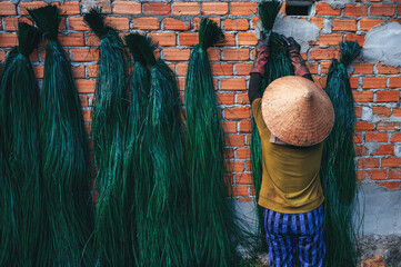 Vietnamese woman in straw hat dries dyed green reeds at a woven mat factory in village in Vietnam