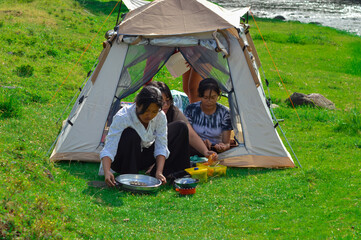 Four teenage girls prepare sausage skewers while others gather ingredients and set up a portable...