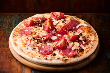 Pizza with ham, salami, tomatoes and mozzarella cheese. Rustic wooden background. Soft focus. Close up.	