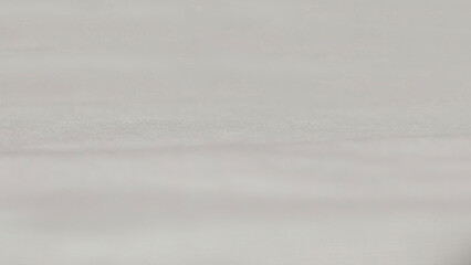 Close-up, abstract image of a soft, fabric textured white surface. The image has very shallow depth of field, with the focus on narrow horizontal