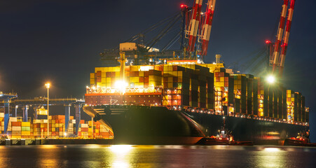 A massive container ship unloading at a container terminal in a seaport at night