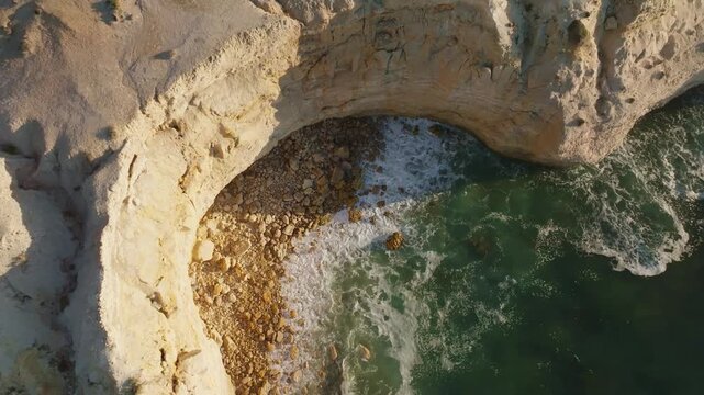 Aerial view of the rugged Port Willunga coastline where the ochre-colored cliffs meet the turquoise ocean, creating a stunning contrast, Port Willunga, South Australia, Australia.