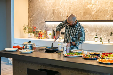 Man is cooking at the modern kitchen with healthy food and various ingredients on the table. Food preparation as a hobby