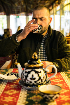A man drinking tea from a traditional pialla at a cafe or restaurant with oriental patterns, capturing the authentic atmosphere
