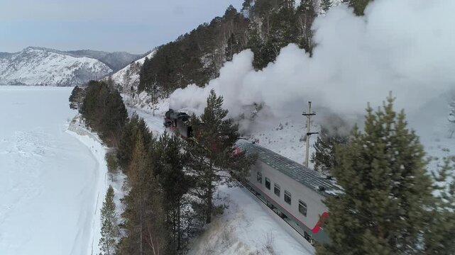 Aerial steam locomotive emitting thick smoke from chimney on sunny winter day. Circum-Baikal railway in Siberia Russia, historical train moving through mountains, unique northern best travel tourism