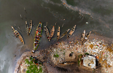 Aerial view of boats clustered near a trash-strewn shore, where the water's surface reflects an oily sheen, casting a somber tone over Buguma, Rivers State, Nigeria.