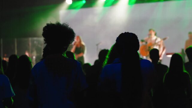 Worshiping congregation silhouetted against emerald stage lights, singing passionately during high-energy christian music event