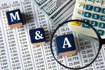 M and A - acronym on wooden cubes against the background of banknotes and calculator