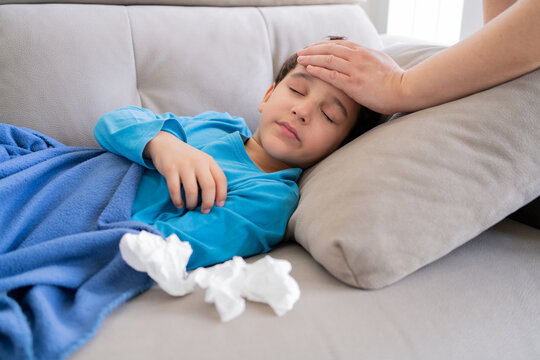 Flu, fever and mother with sick boy for health, virus or infection symptoms in bedroom. Family, childcare and hand of parent with child at home in couch to check temperature for cold, illness and flu - Powered by Adobe
