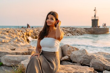 Young Woman Sitting on Rocks by the Sea at Sunset
