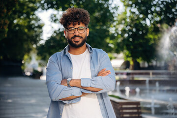 Arms crossed, standing. Handsome man is outdoors in the city