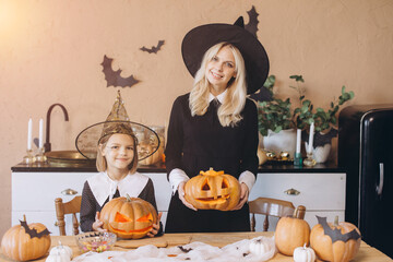 Mother and daughter showing carved pumpkins wearing witch costumes during Halloween party