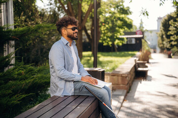 Fototapeta premium Sitting and reading using Braille. Blind man with white cane and sunglasses is in the city