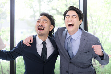 新緑の窓が綺麗なオフィスでビジネスマン肩を組む　達成や成功のイメージ