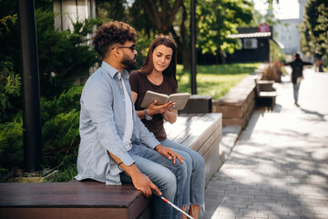 Fototapeta premium Woman is with blind man, sitting outdoors and reading book
