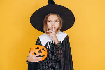 Little witch holding pumpkin basket making silence gesture on yellow background