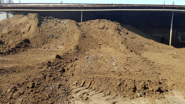 A large stock of olive pomace, or 'olive core,' piled up inside a factory building after the olive oil extraction process, used for biomass or other purposes.