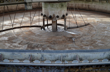 A wide shot of an empty, circular sedimentation tank at a wastewater treatment plant, revealing the industrial machinery and concrete structure used for water clarification.