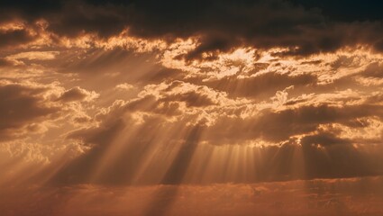 Golden sunlight breaking through dark clouds in dramatic sky during sunset or sunrise with visible sun rays and warm orange hues in atmospheric scene