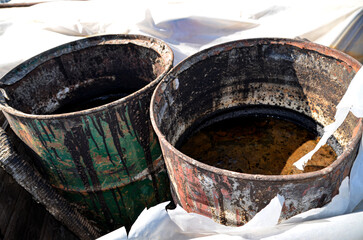 Collected waste oil and water are deposited in two rusty metal barrels, showing a scene of...