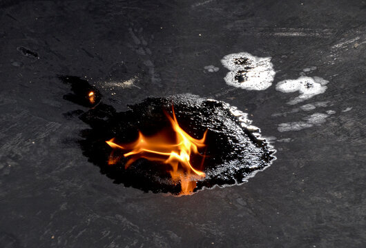 A burn test on a puddle of fuel produced from recycled waste tires, with flames rising to show its flammability as an alternative energy source.
